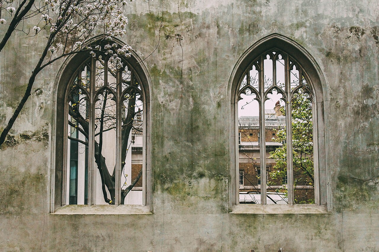 Two pointed Gothic windows in the weathered church wall at St Dunstan in the East, framed by flowering branches and spring greenery.